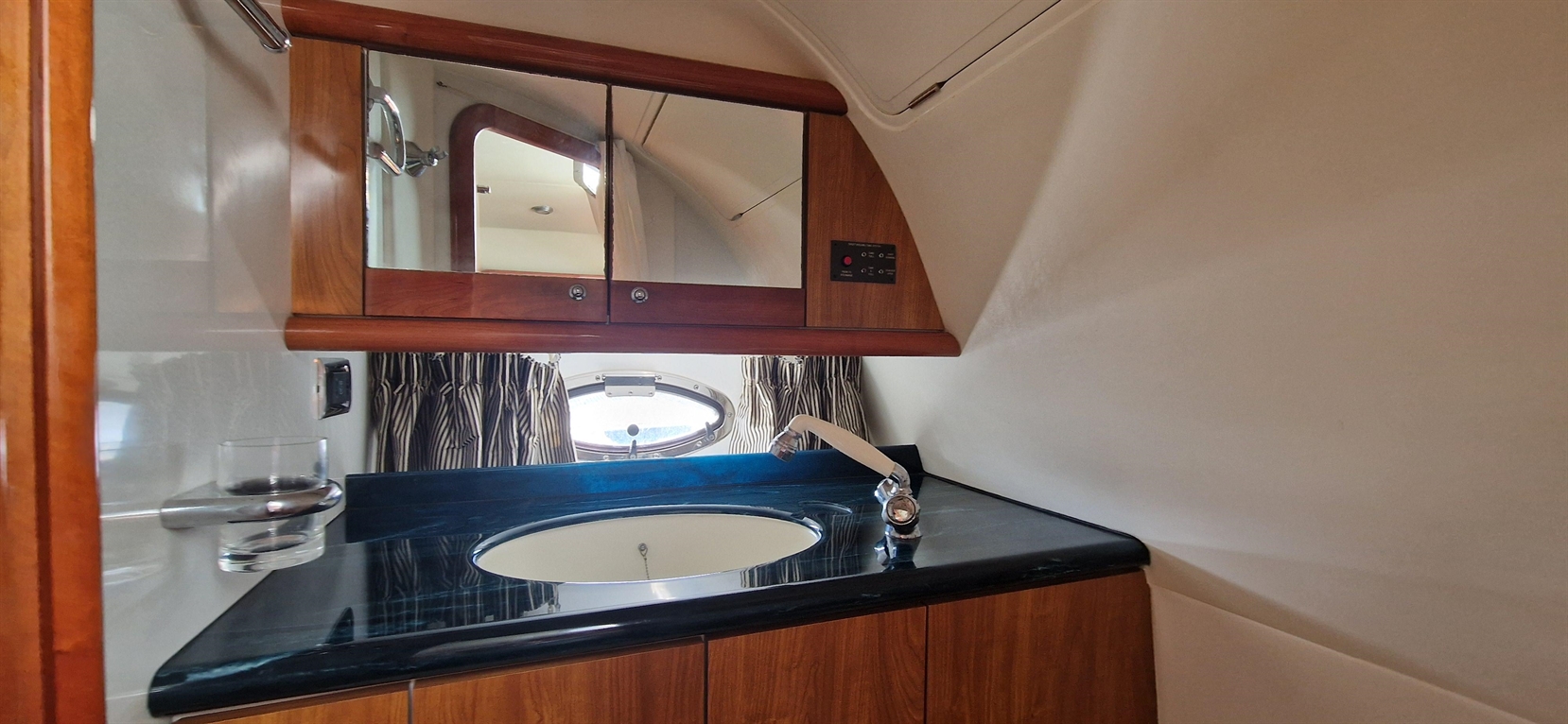 Sleek boat bathroom featuring a sink, mirror, striped curtains, and a porthole, emphasizing nautical design and functionality.
